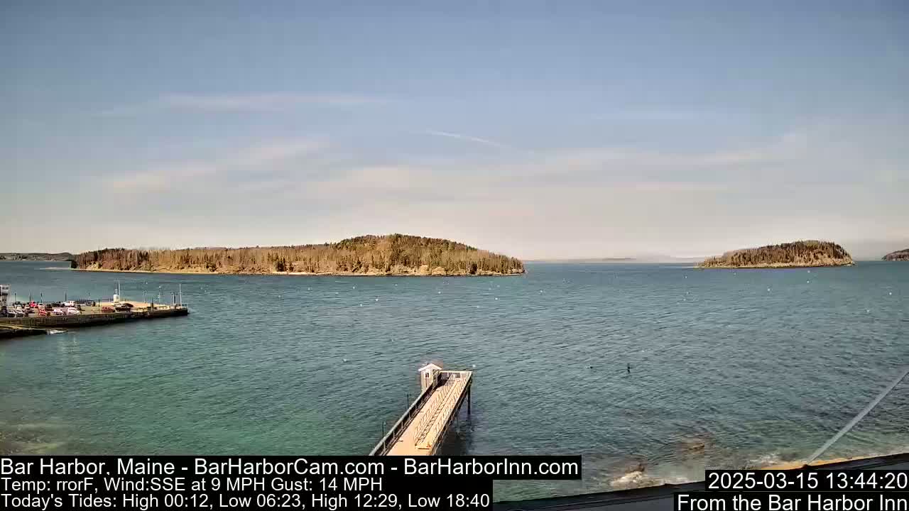 A long pier extends into a calm body of water, with several islands visible in the distance under a mostly clear sky.
