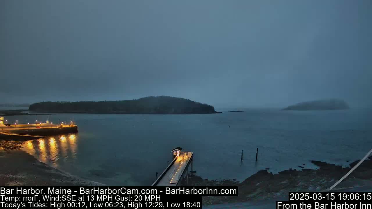 A long pier extends into a calm, gray harbor under an overcast sky, with a small island visible in the distance.