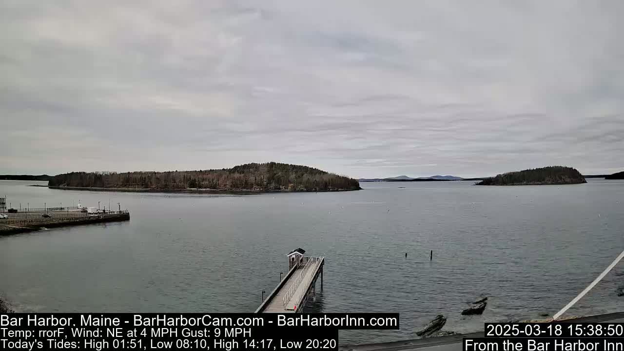 A long pier extends into a calm bay under an overcast sky, with several wooded islands visible in the distance.