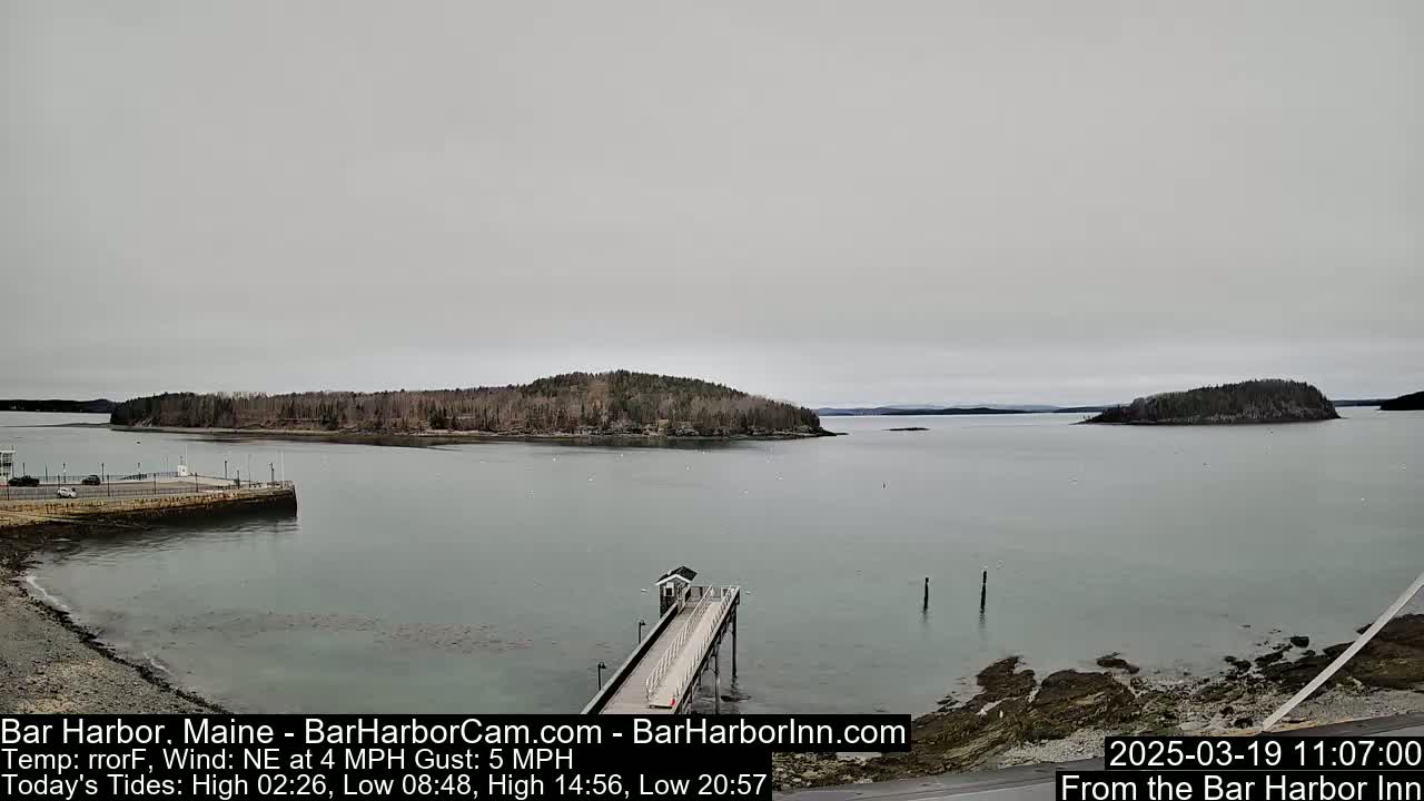 A calm, overcast day reveals a harbor scene with a long pier extending into the water, two small islands in the distance, and a rocky shoreline.