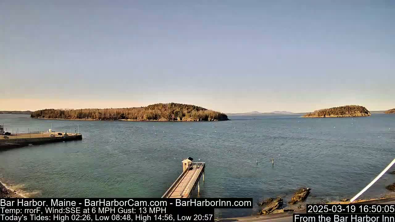 A calm body of water with several small islands and a long pier extending from the shoreline under a clear, sunny sky.