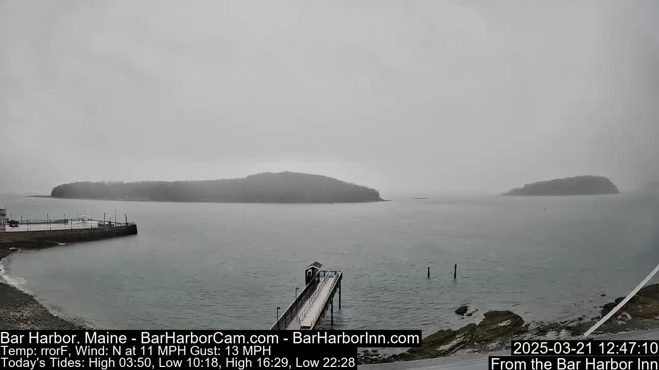 A hazy, overcast day shows a gray-blue body of water with two small islands in the distance and a long pier extending from a rocky shoreline.