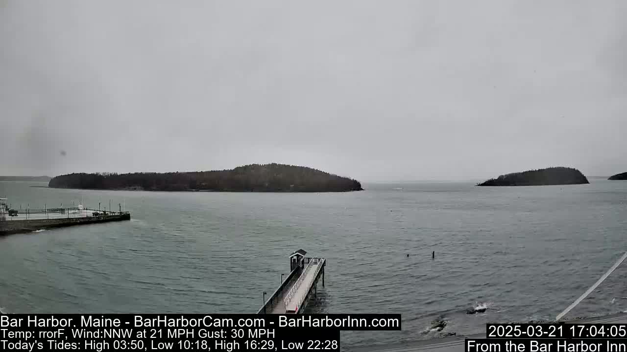 A gray, overcast day shows a harbor with a long pier extending into the water, two small islands in the distance, and calm water.
