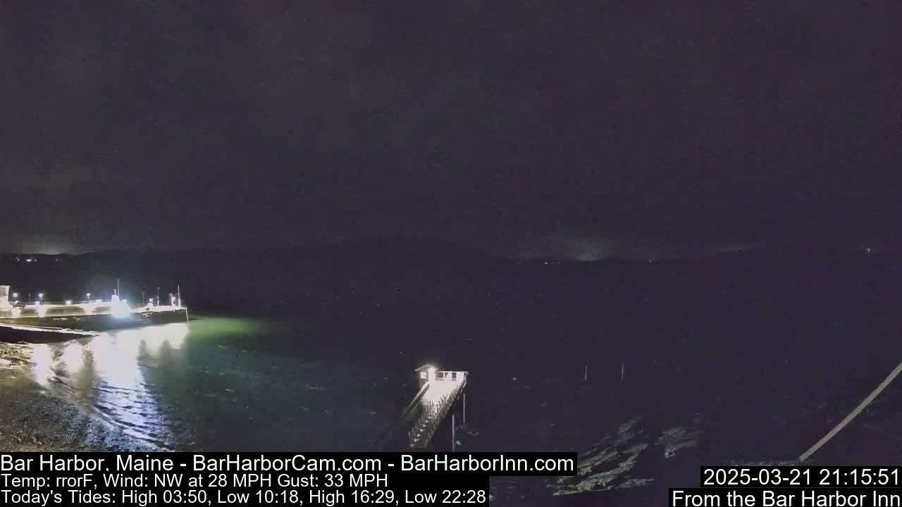 A nighttime, dark view of a harbor with a pier and a boat, under a windy sky.