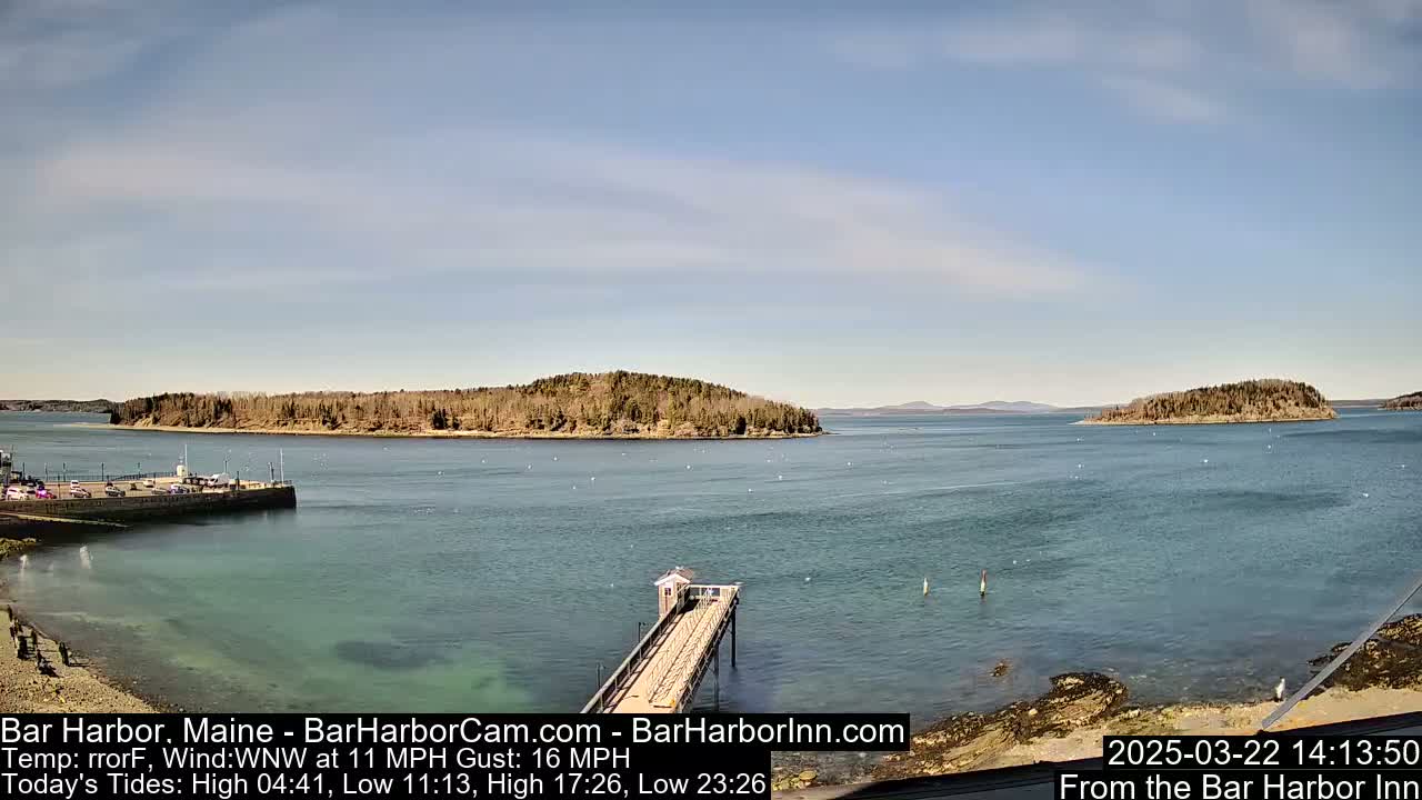 A partly sunny day shows a view of a calm body of water with several islands in the distance, a pier extending into the water from a rocky shoreline, and a parking area.