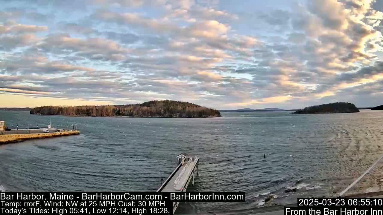 A long pier extends into a choppy body of water under a partly cloudy sky, with islands visible in the distance.