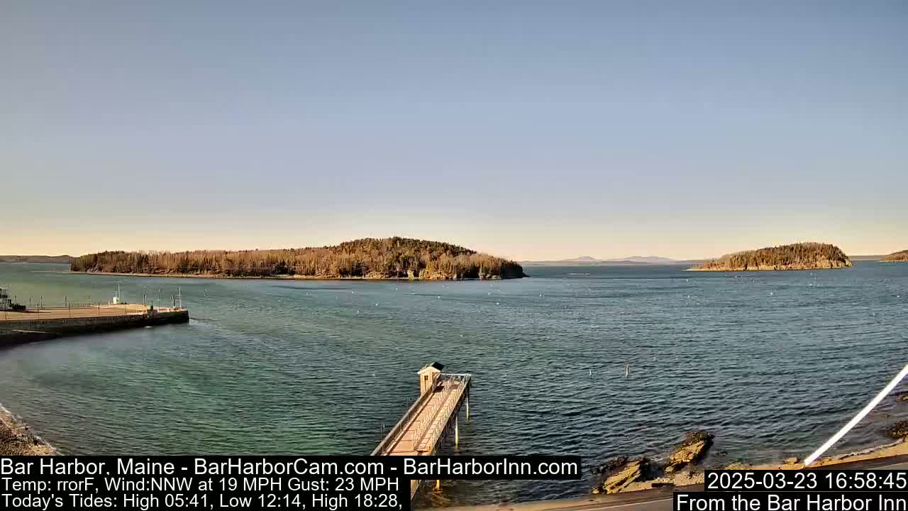 A calm body of water with islands and a long pier extends into it under a clear, bright sky.