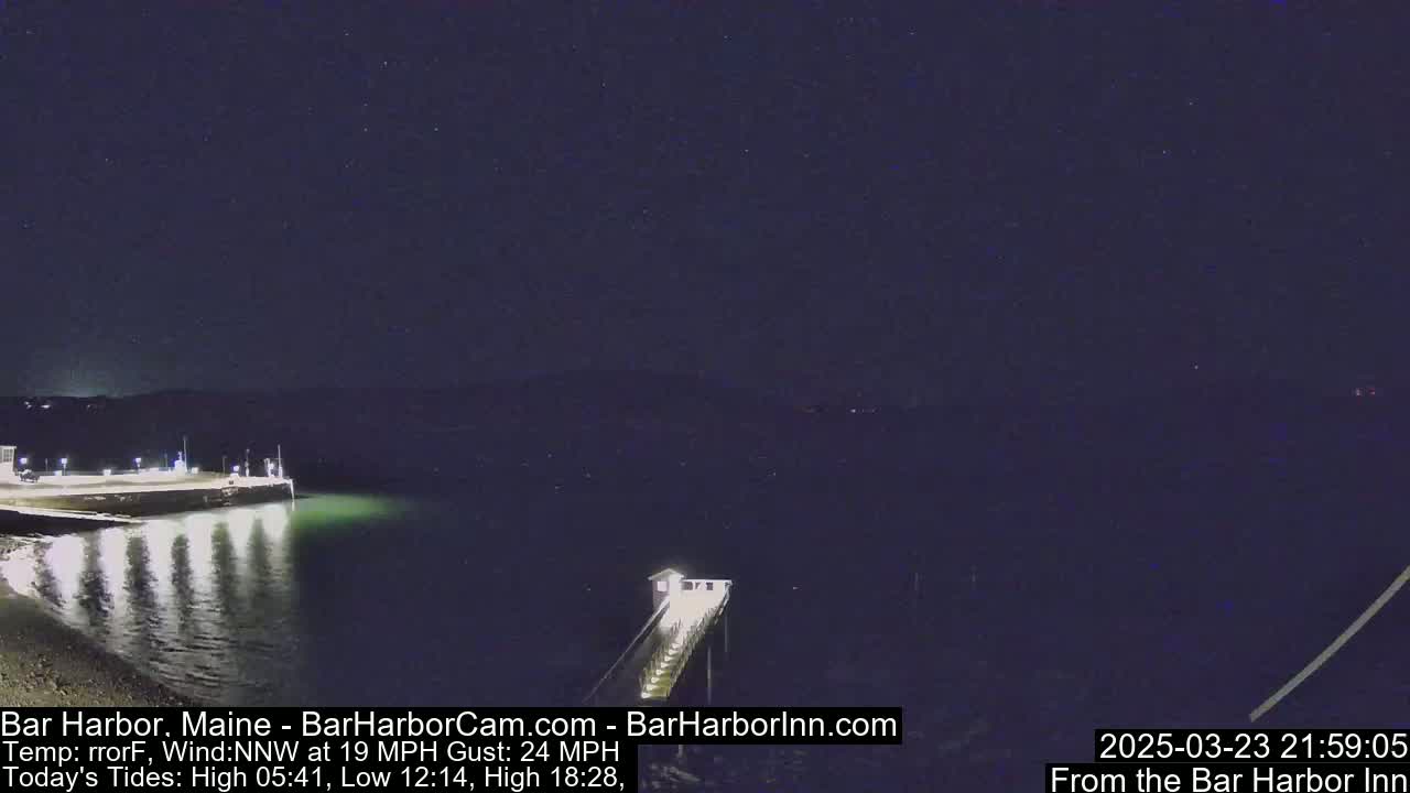 A nighttime view of a calm harbor with a pier extending into the water under a starry sky, with a northwest wind at 19 mph and gusts up to 24 mph.