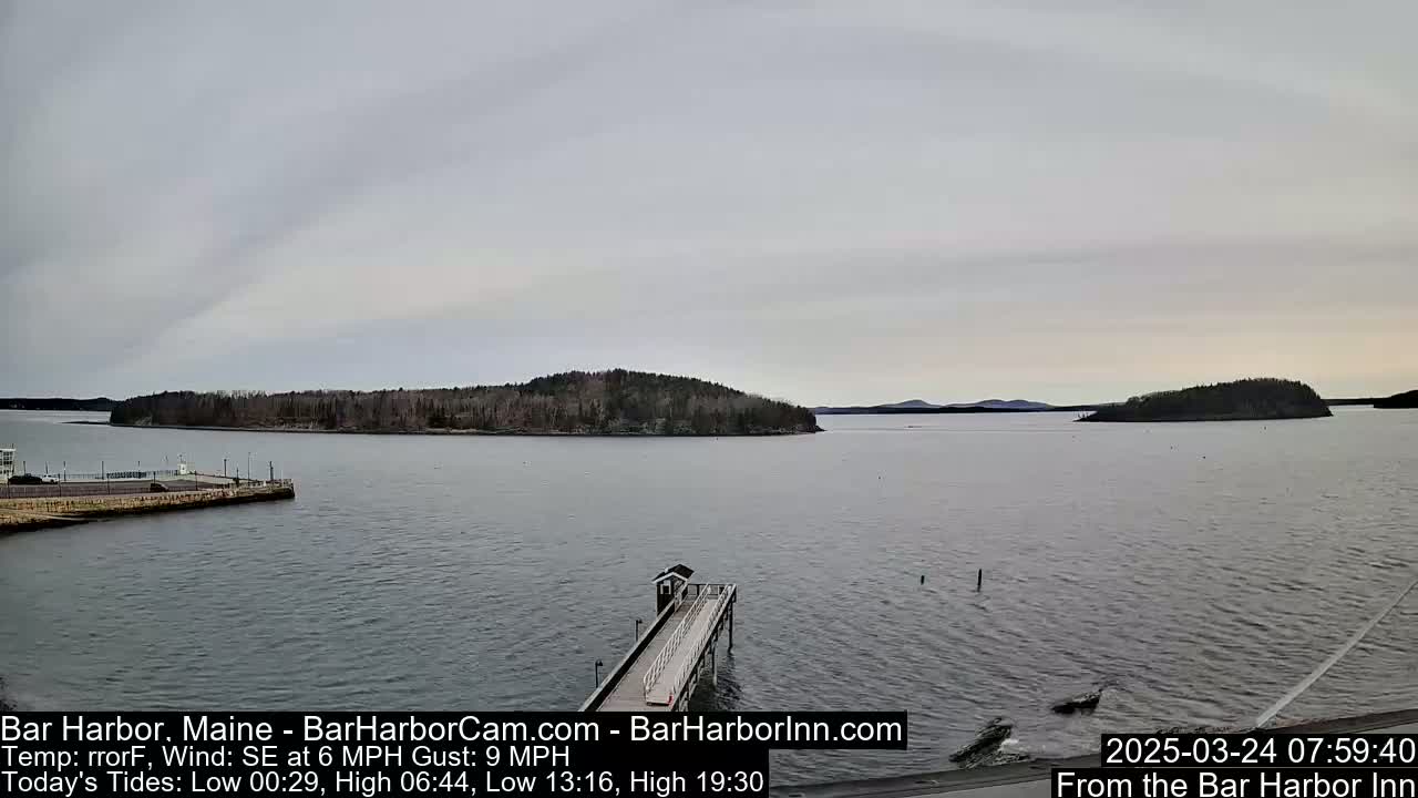 A long pier extends into a calm, gray body of water, with several small islands in the background under an overcast sky.