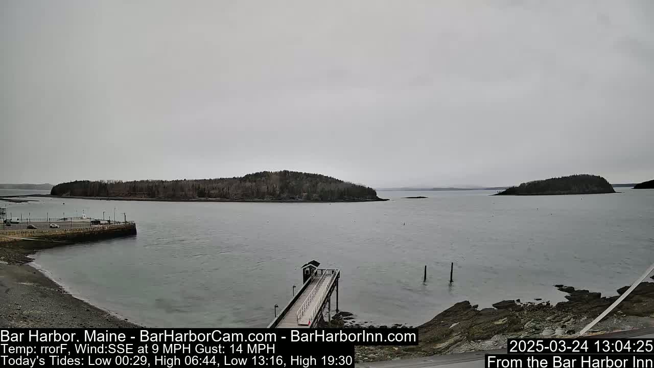A gray, overcast day shows a calm body of water with several small islands in the distance and a long pier extending into the water from a rocky shoreline.
