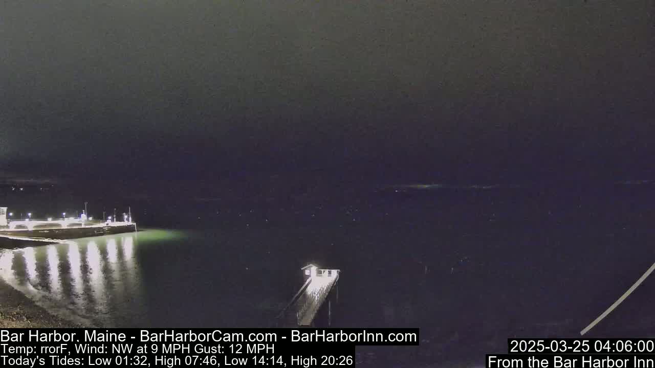 A nighttime, low-light view of a harbor with a pier extending into the water under a dark sky, with a northwest wind at 9 mph and gusts up to 12 mph.