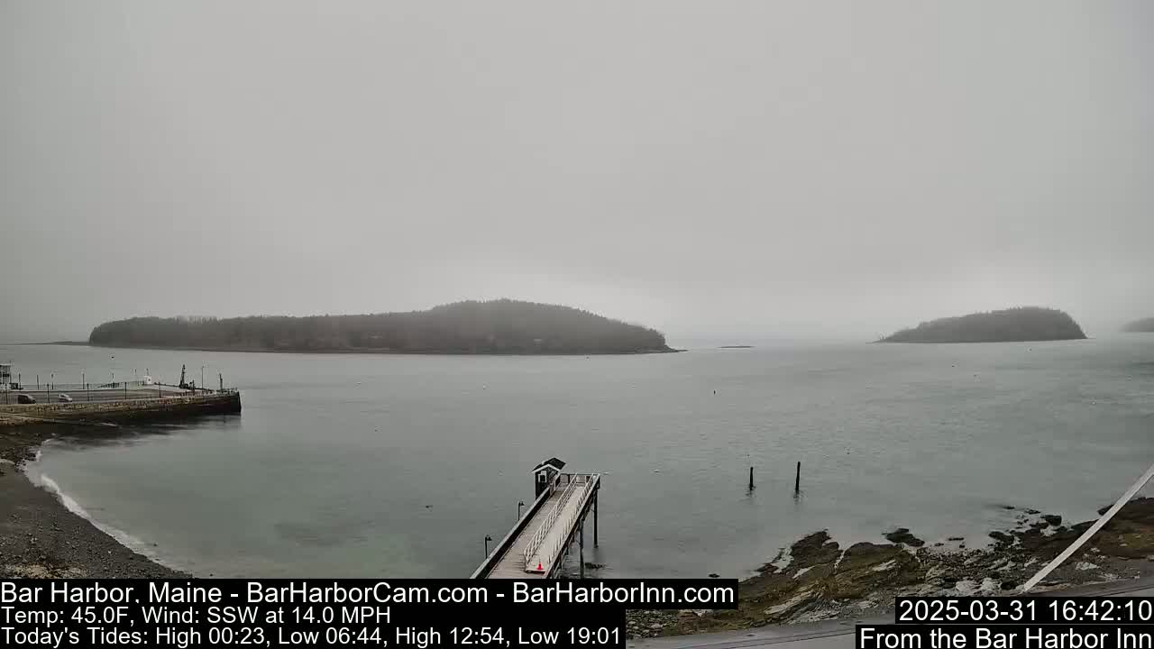 A hazy, overcast day reveals a calm harbor scene with a long pier extending into the water, and several small islands in the distance.