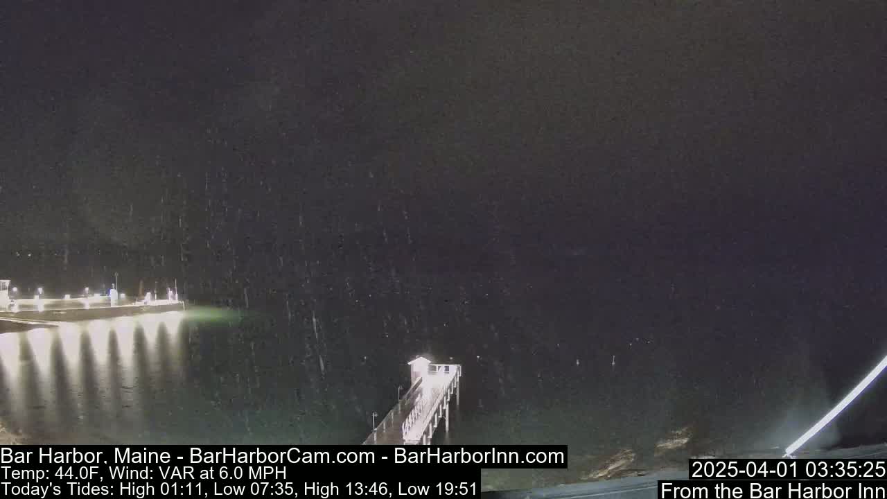 A nighttime view of a pier extending into dark water under light snow.