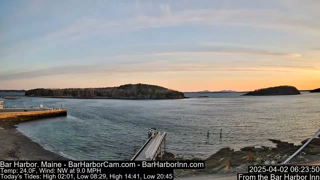 A calm harbor at sunset, with a small pier extending into the water, under a mostly clear sky.