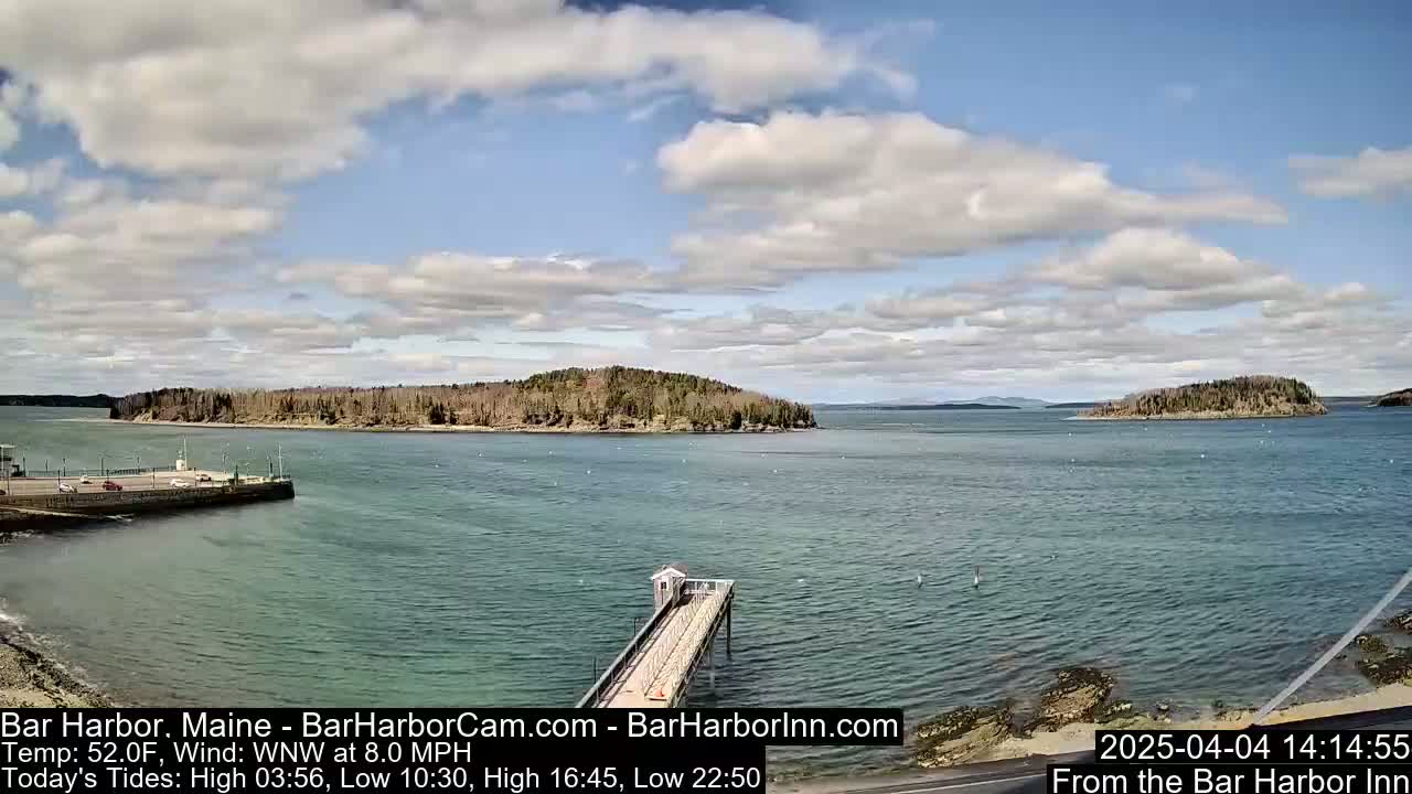 A partly cloudy day shows a view of a calm body of water with islands and a long pier extending into it.