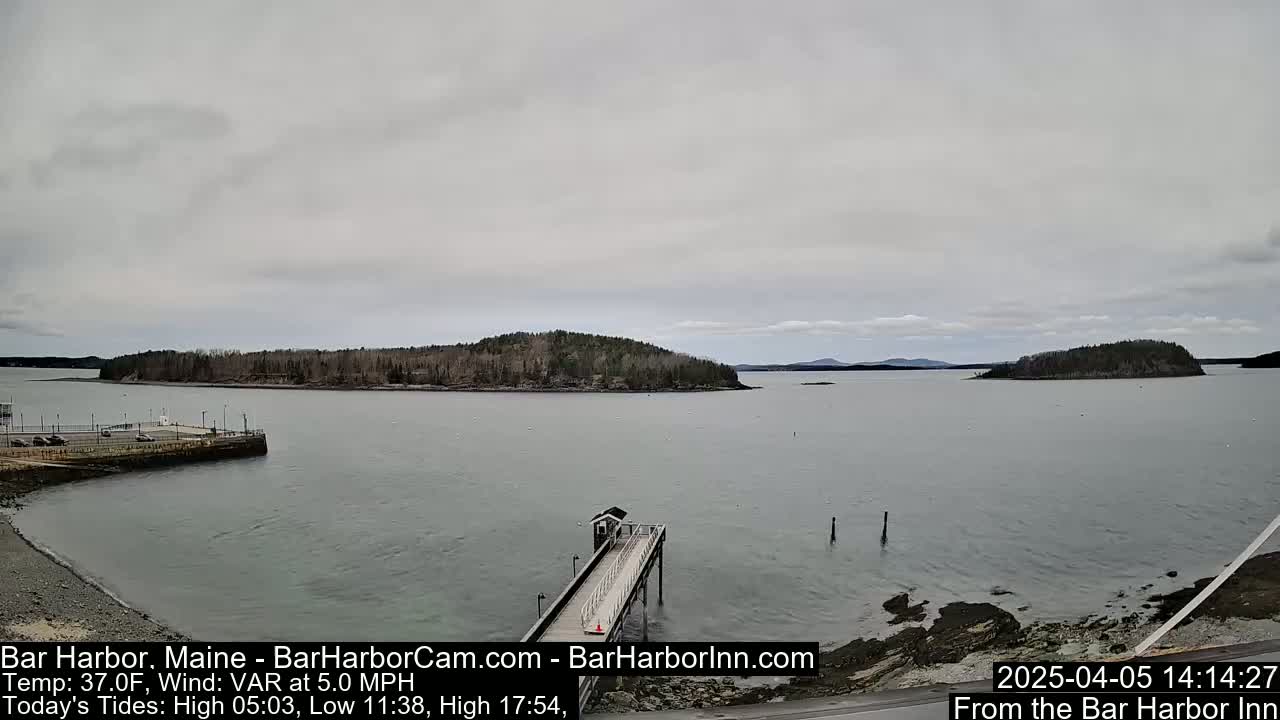 A long pier extends into a calm body of water under an overcast sky, with several islands visible in the distance.