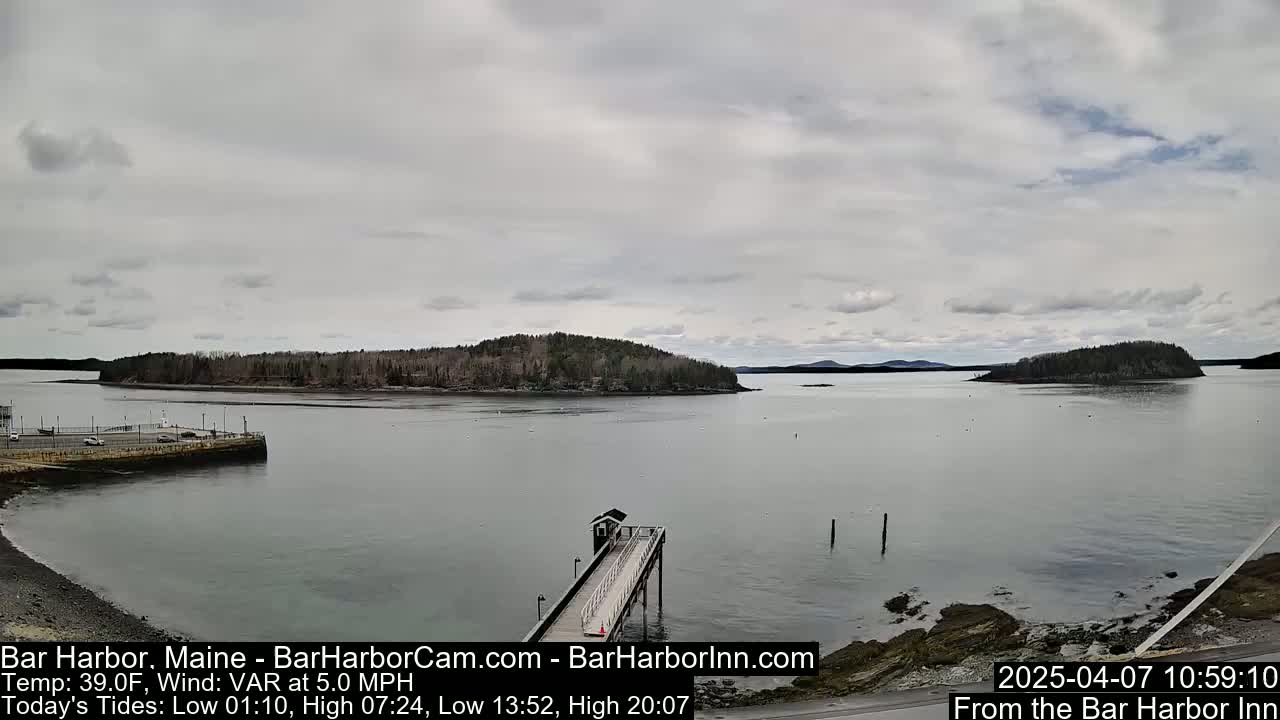 A calm, overcast day shows a view of a harbor with a long pier extending into the water, and several small islands in the distance.