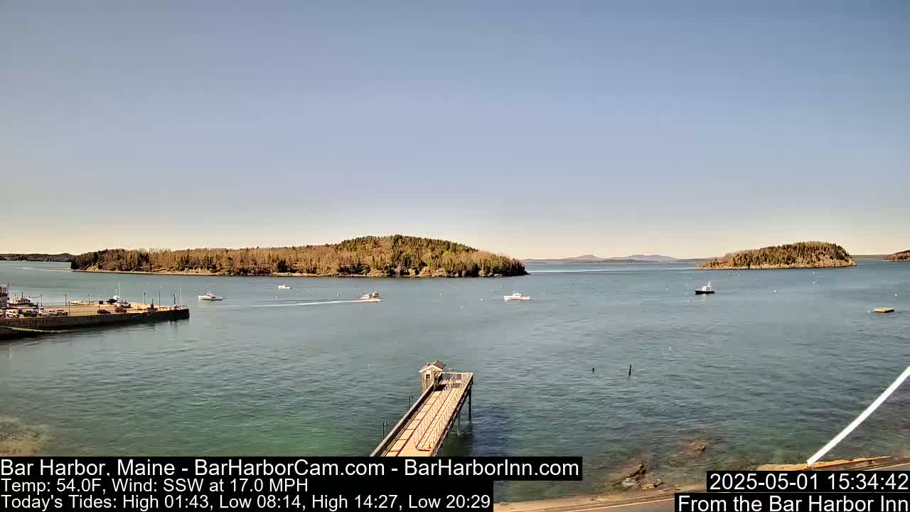 A calm, sunny day reveals a harbor with several boats, a long pier, and several small islands in the distance.