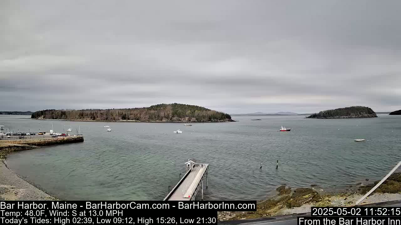 A calm harbor scene shows a long pier extending into the water, with several small boats and islands visible under an overcast sky.