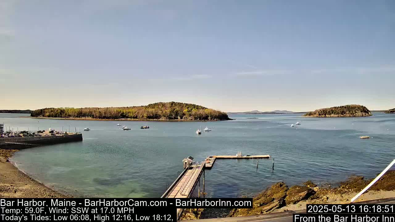 A tranquil harbor scene with several boats, a small pier, and tree-covered islands under a clear, sunny sky.