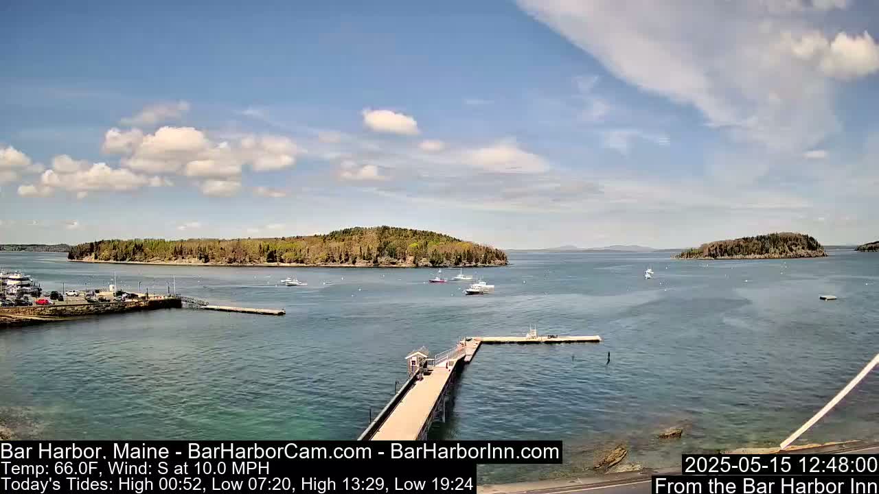 A partly sunny day reveals a harbor scene with several boats and islands, a long pier extending into the water, and a small parking lot.