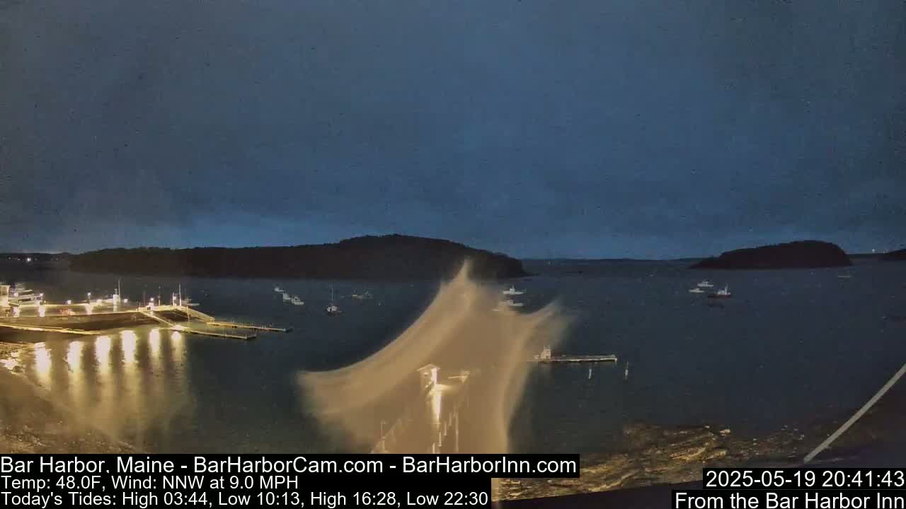 A nighttime harbor scene with several boats moored at a pier under a dark, clear sky and a 9 mph northwest wind.