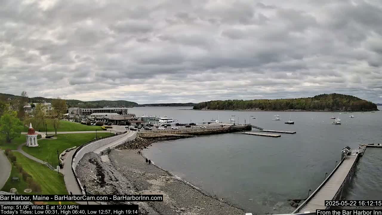 A harbor town on a partly cloudy day, with boats in the water and a stone walkway leading to a pier.