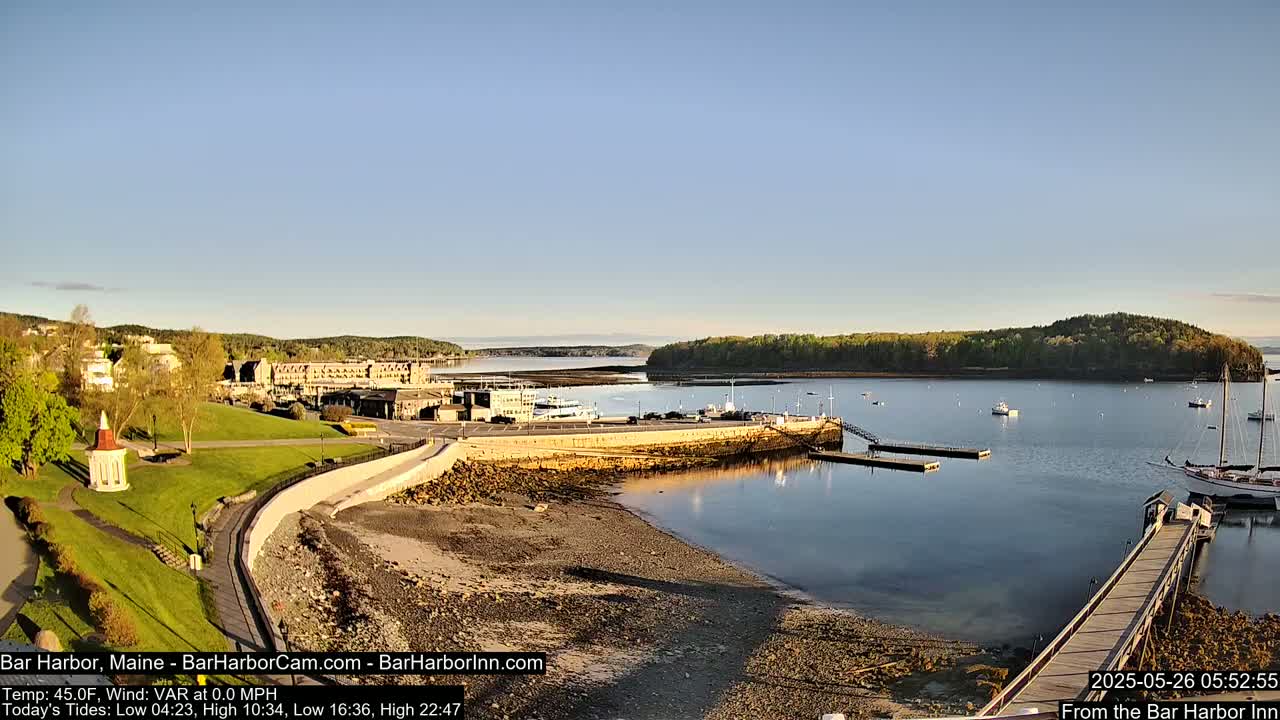 A calm harbor with a few boats, a grassy park, and buildings along the shoreline under a clear blue sky.