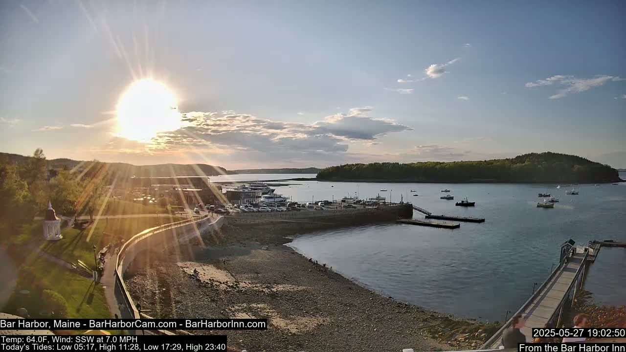 A sunny, partly cloudy sunset over a harbor filled with boats and a town on the shoreline.