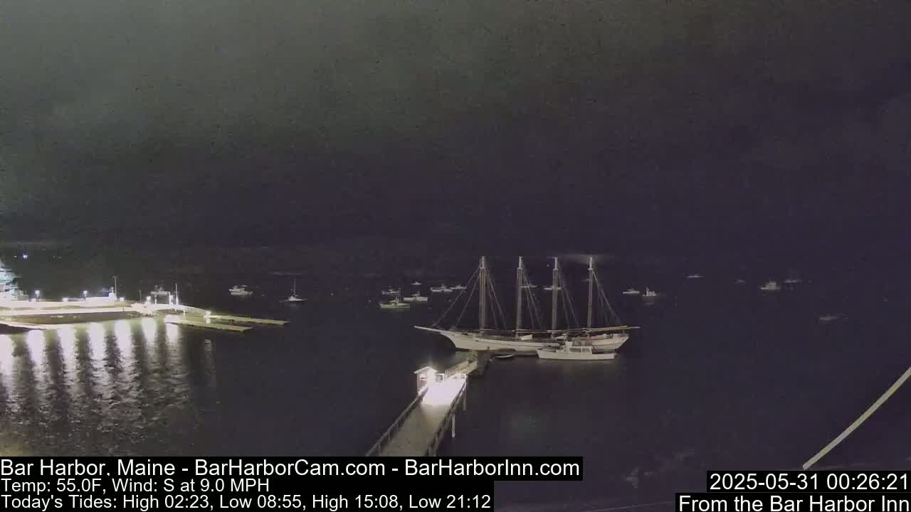 A large sailing ship is docked at a pier at night under a dark, cloudy sky.