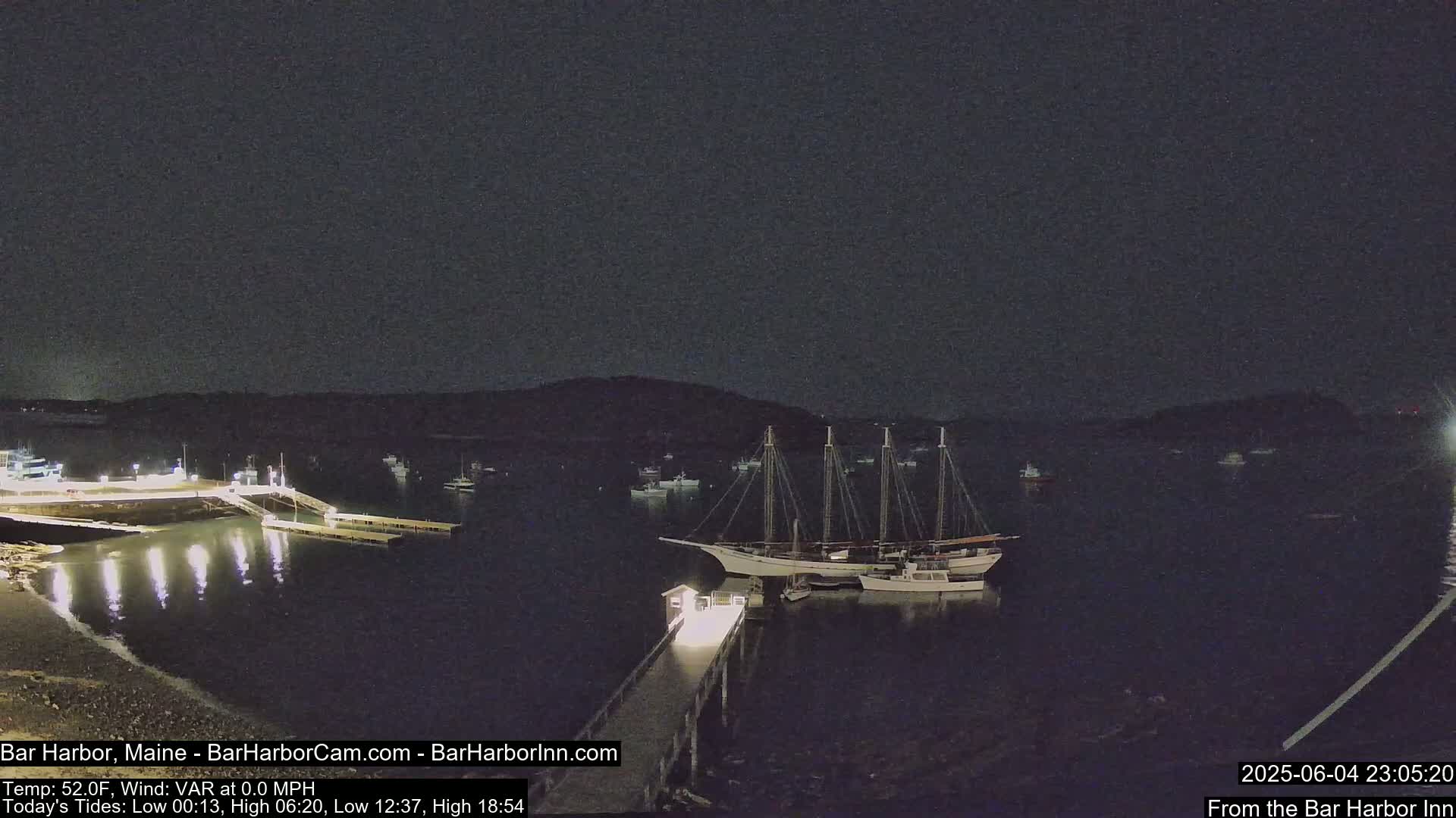 A nighttime harbor scene shows a large sailboat docked at a pier, with several smaller boats in the water and a dark sky.