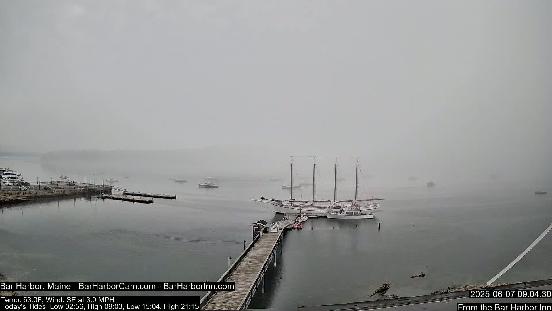 A foggy harbor scene shows a large sailing ship and several smaller boats moored at a pier, with additional boats visible in the distance.