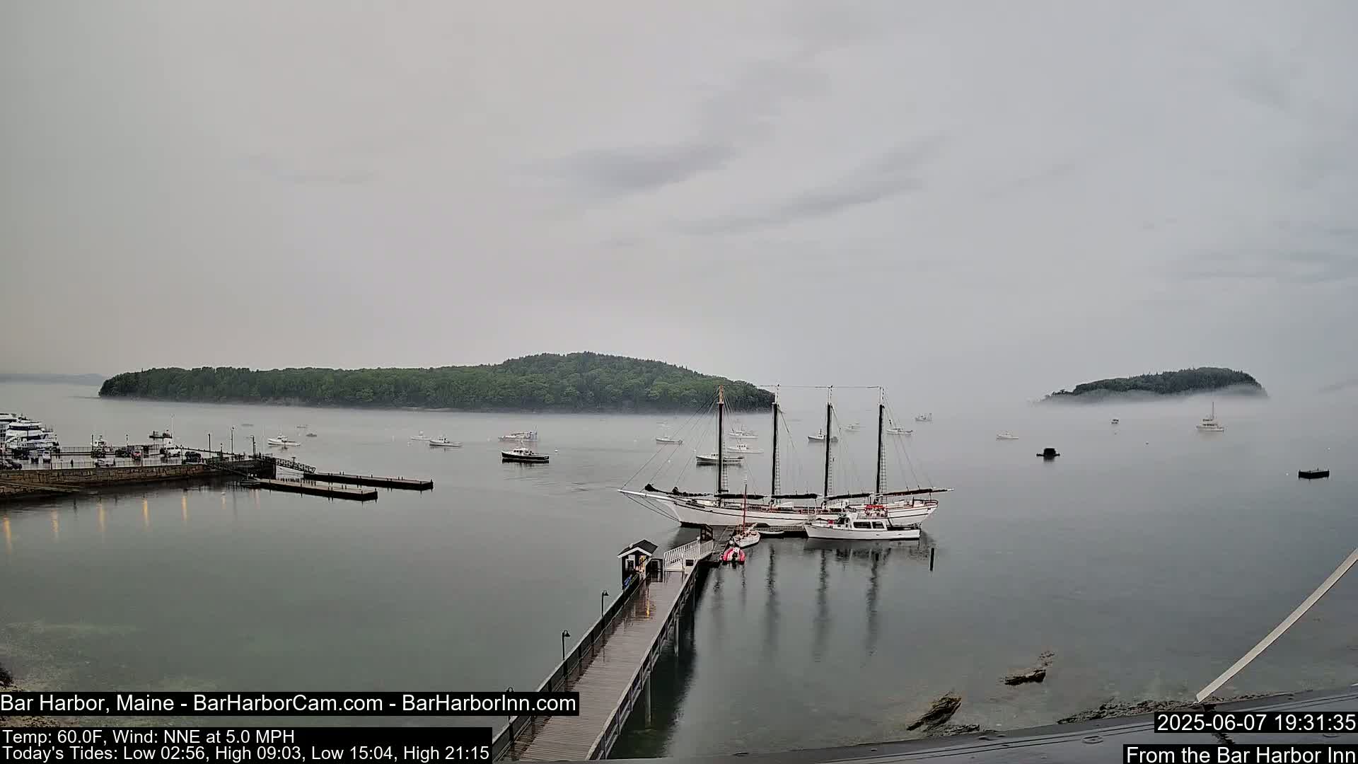 A foggy harbor scene shows several boats, including a large sailing ship docked at a pier, with a small island in the background.
