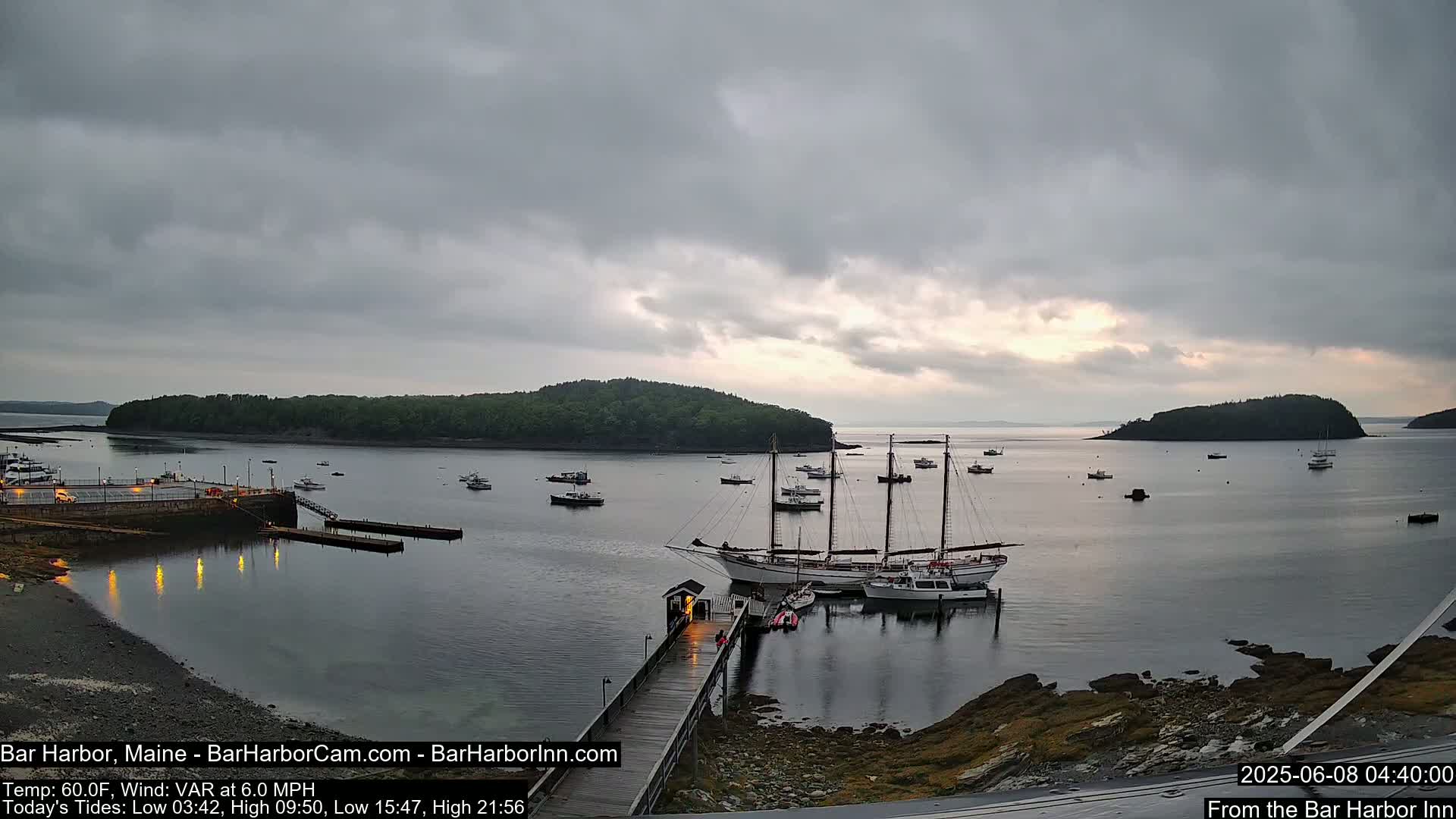 A calm harbor with numerous boats, including a large sailing ship docked at a pier, under an overcast sky.
