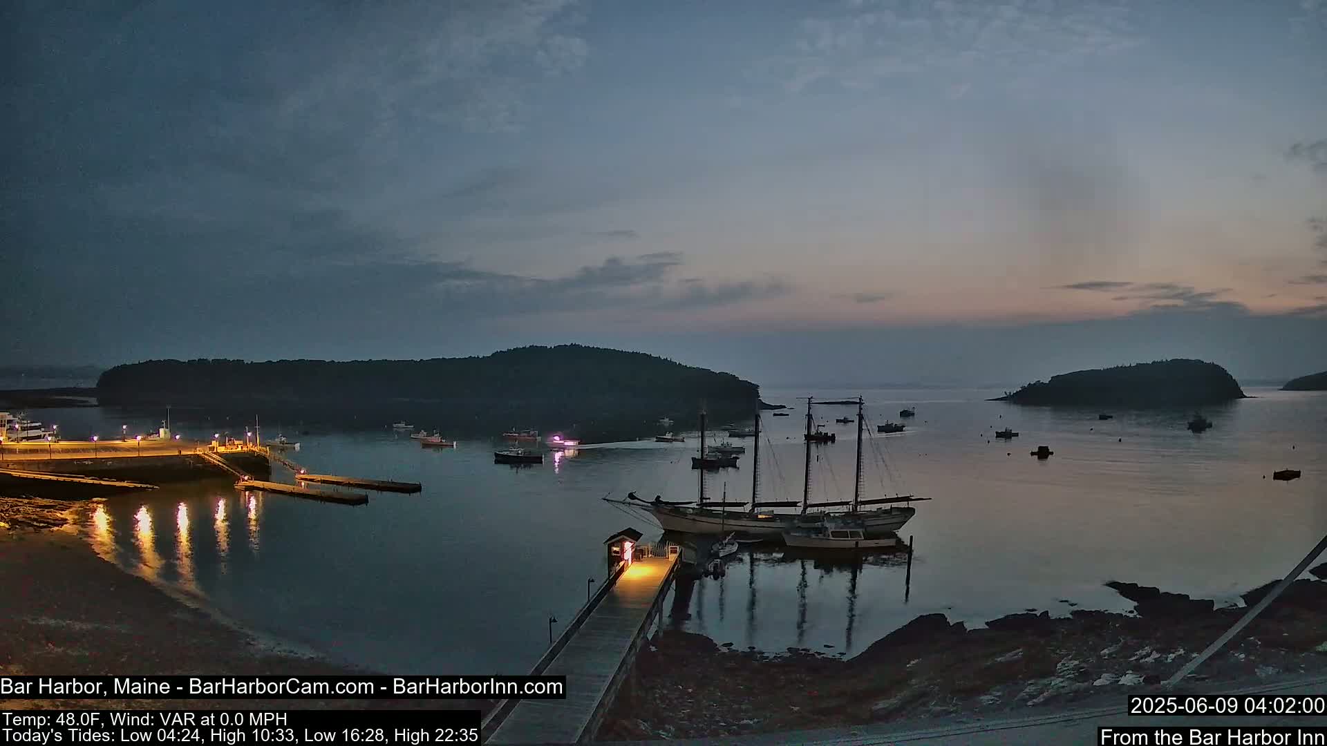 A calm harbor at twilight, with several boats moored at a pier, and islands visible in the distance under a dusky sky.