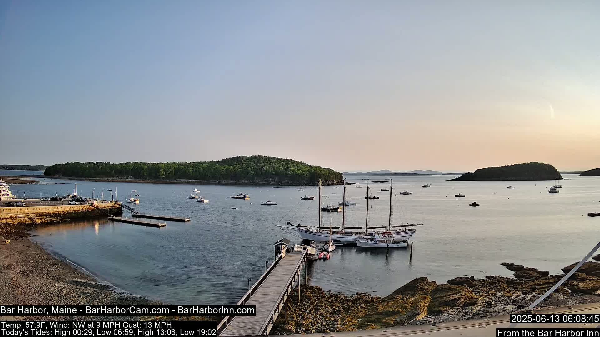 A calm harbor with several boats, including a large sailing ship, is seen at sunset under a clear sky.