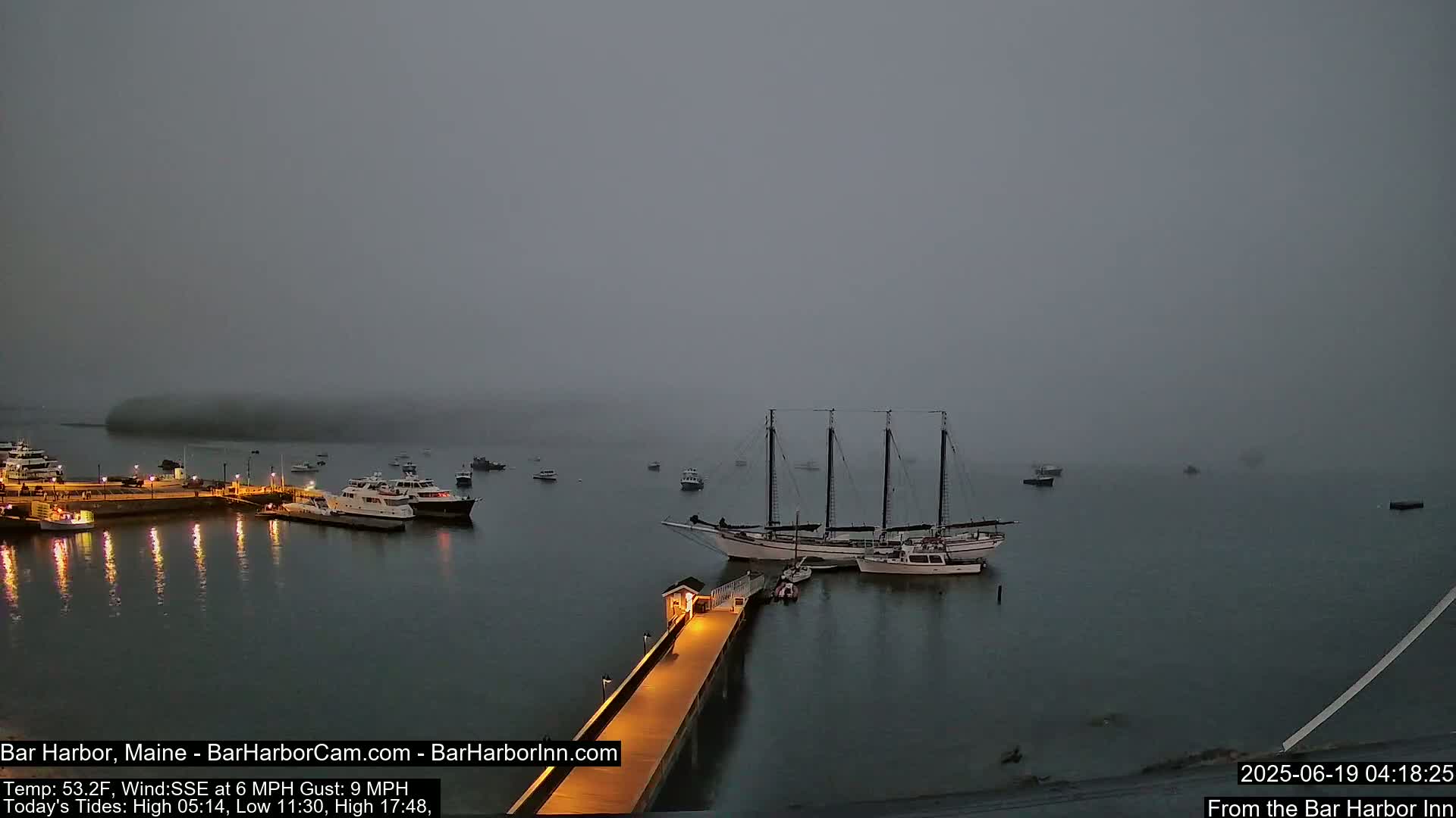 A large sailing ship is moored at a pier in a foggy harbor with several smaller boats nearby.
