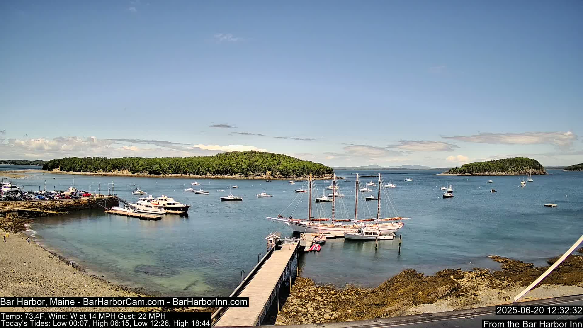 A harbor filled with numerous boats, including several large sailing ships, is situated under a mostly clear, sunny sky.