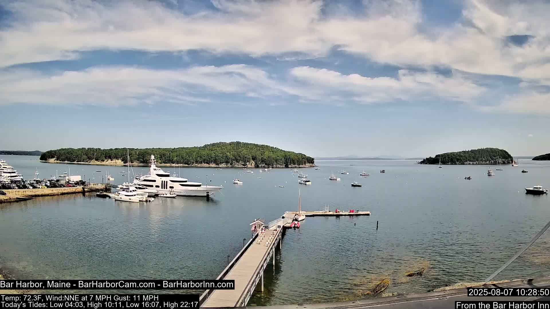 A harbor filled with numerous boats, including a large yacht, is shown under a partly cloudy sky.