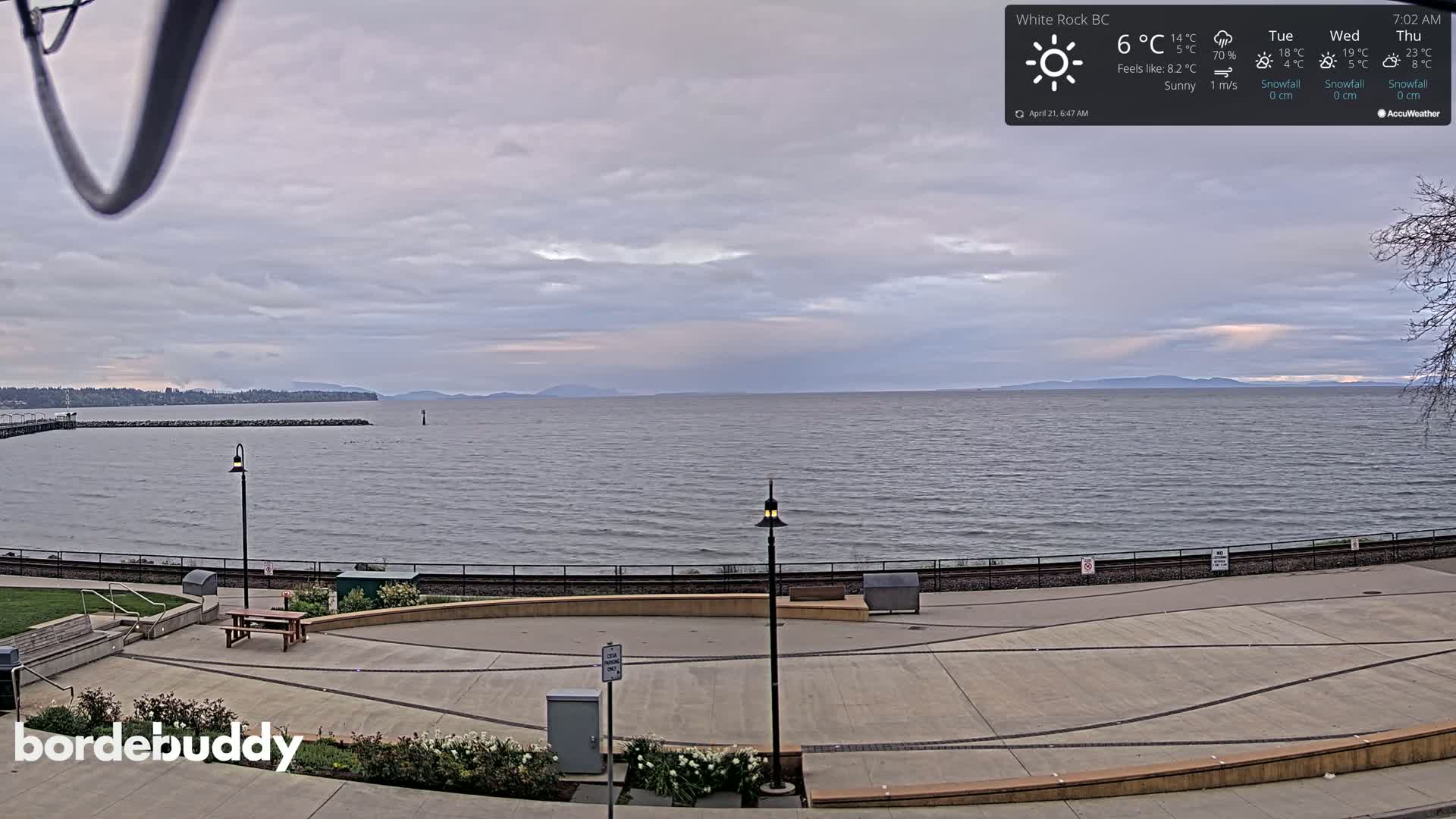 A sunny, but cloudy, ocean view from a paved waterfront area with lamp posts and benches.