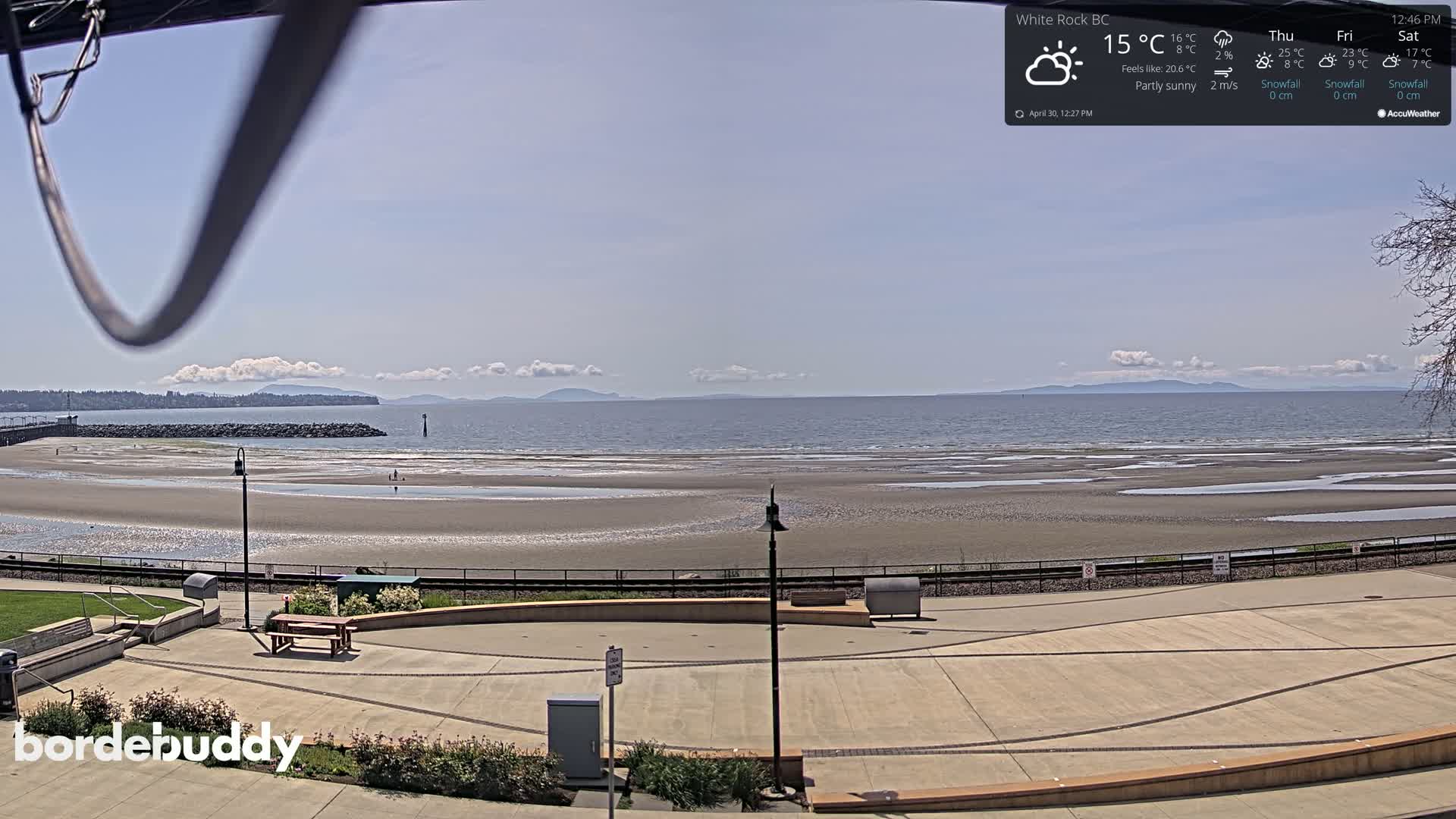 A partly sunny beach scene overlooks a calm ocean with distant mountains under a clear sky.