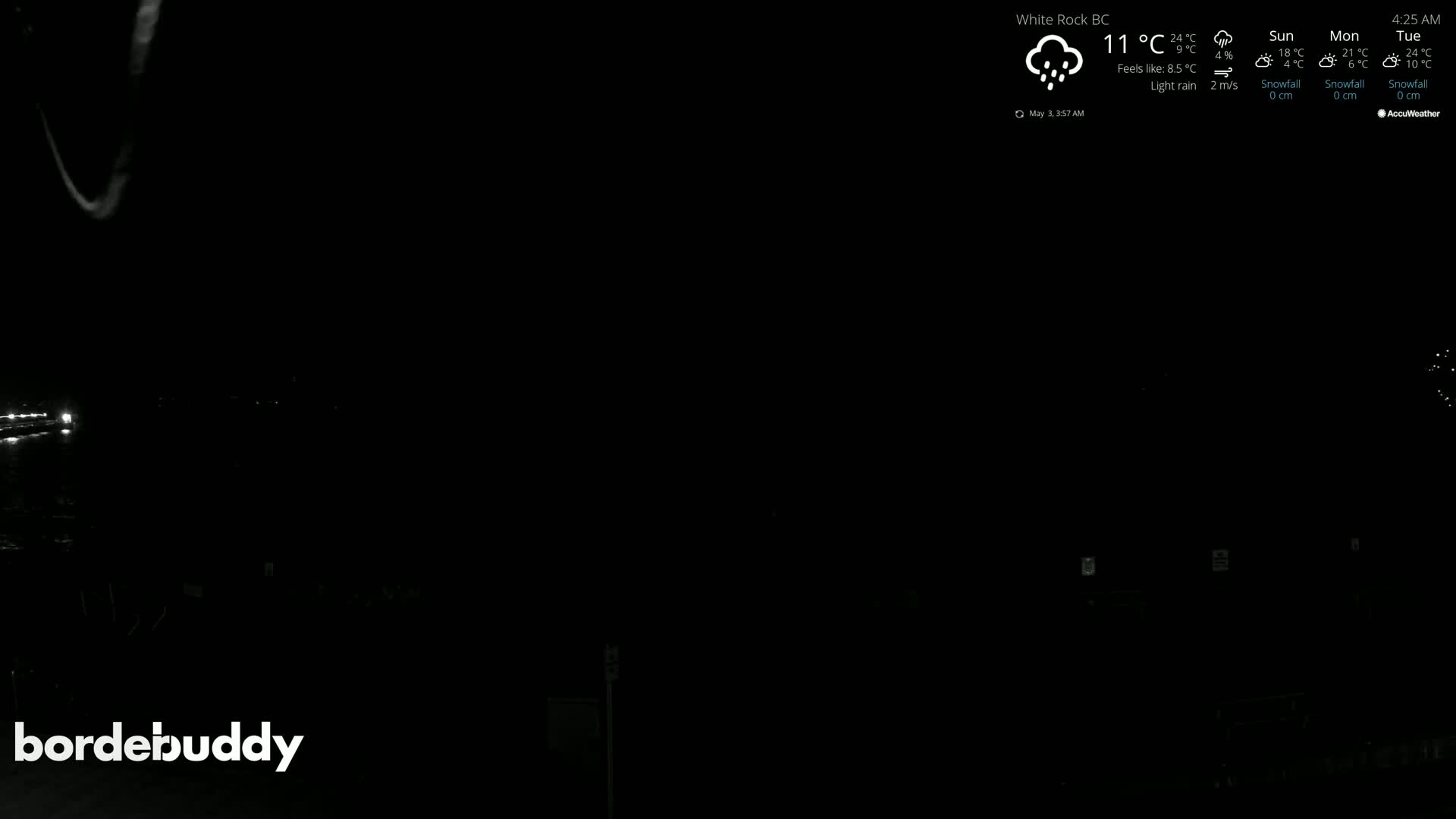 A dark, nighttime scene with light rain shows a few faintly visible lights in the distance.