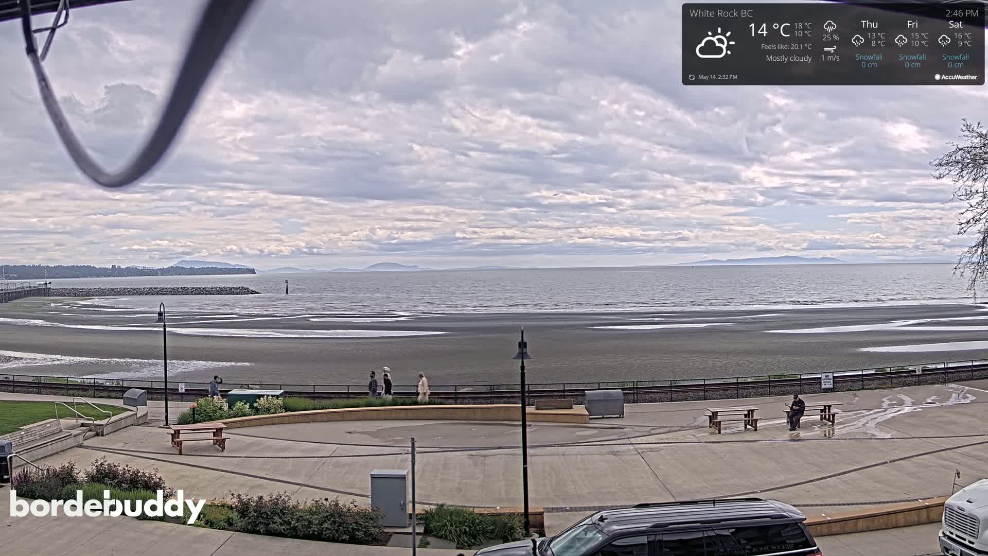 A mostly cloudy day shows a wide sandy beach and calm ocean with distant mountains under a mostly cloudy sky.