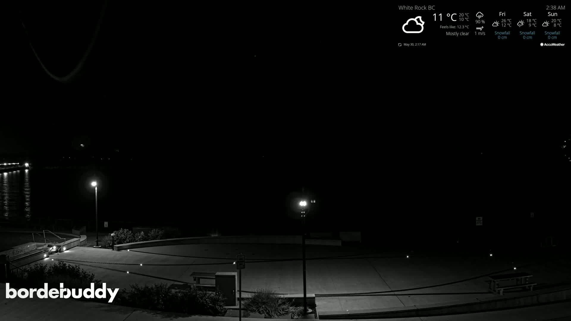 A mostly clear night scene shows a dark paved area with several lights, near a body of water.