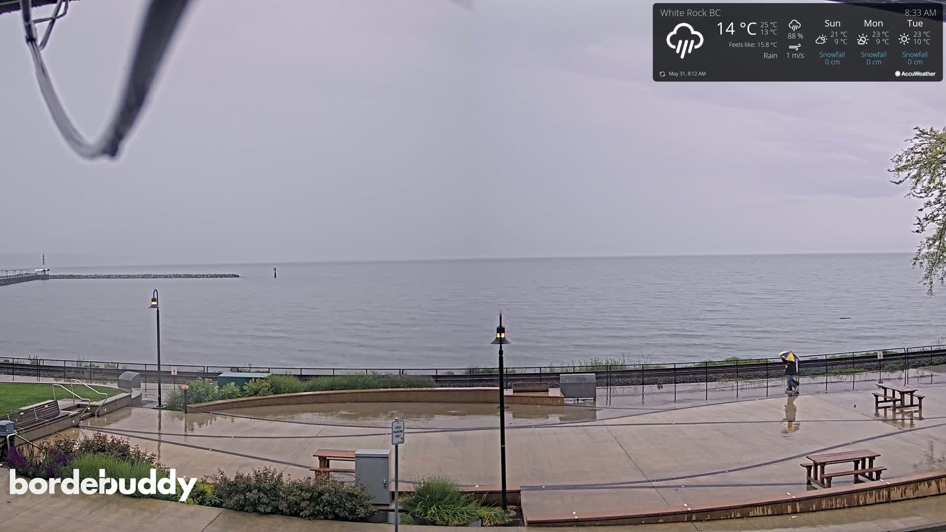 A rain-slicked waterfront plaza overlooks a calm, gray sea under an overcast sky.
