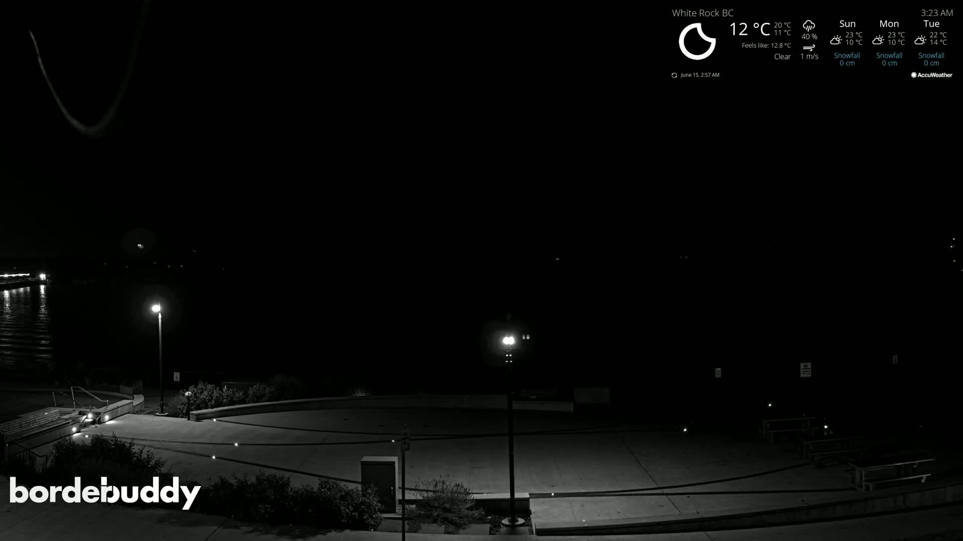 A nighttime, clear-weather view of an empty plaza next to a body of water, illuminated by several lampposts.
