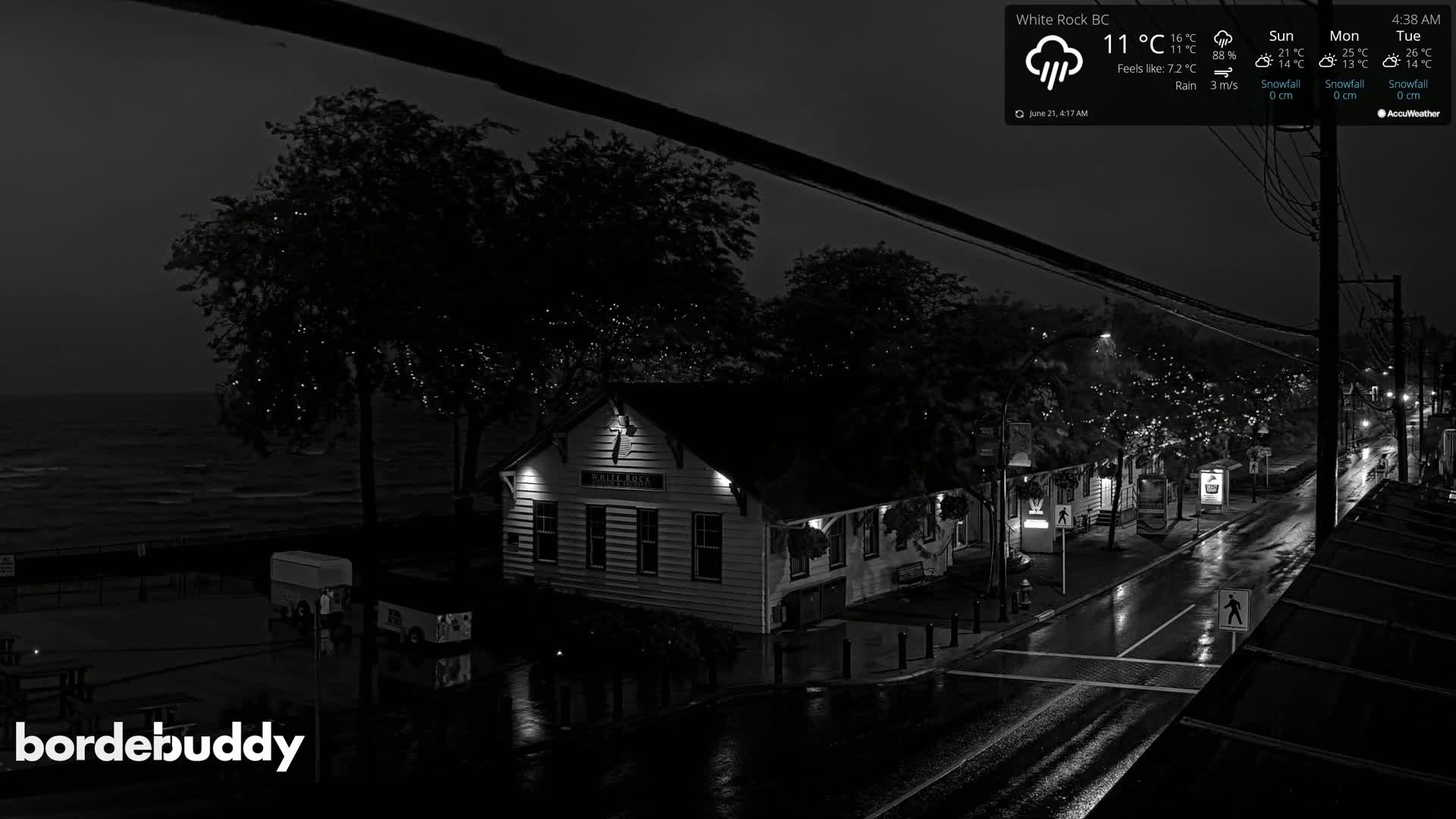 A rain-slicked nighttime street scene shows a building near the ocean under a cloudy sky.