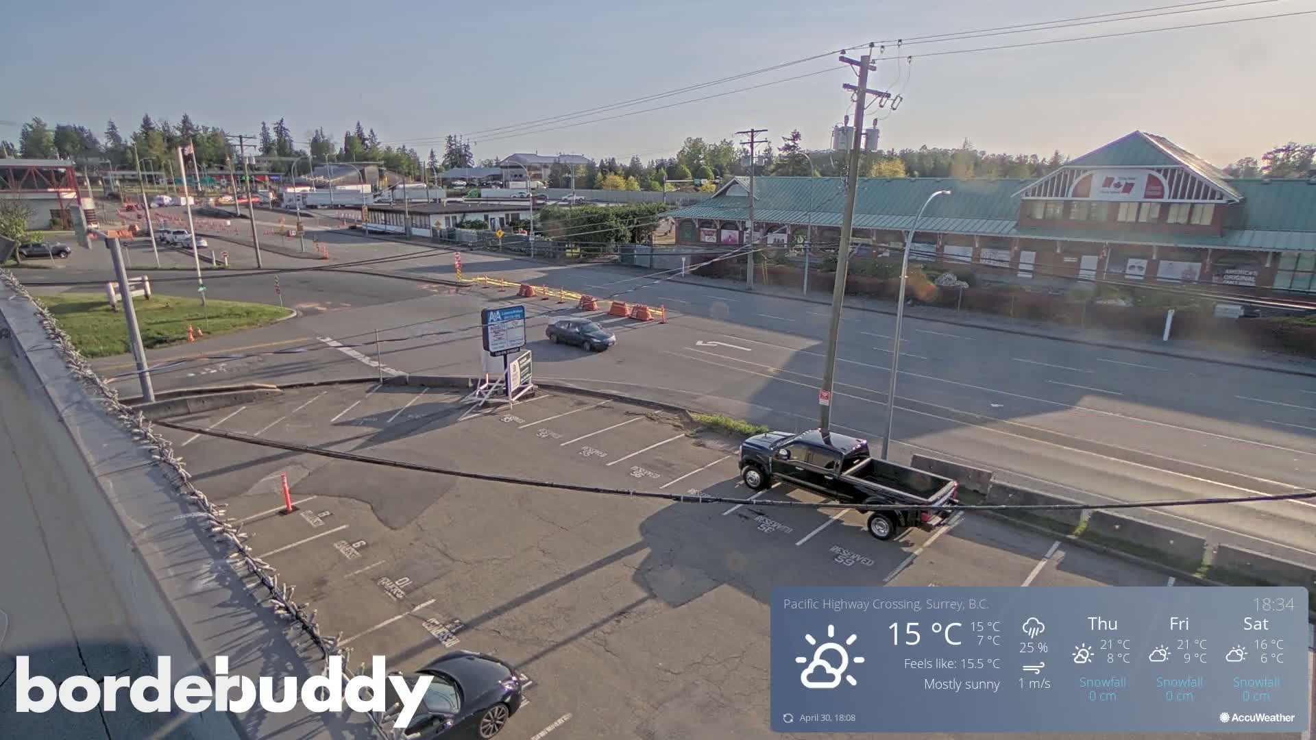 A mostly sunny overhead view of a highway crossing, with a parking lot, some cars, and buildings including a large commercial structure.
