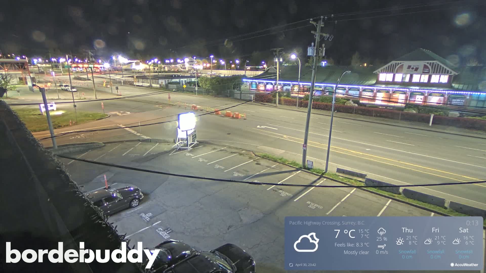 A mostly clear night scene shows a street intersection with parked cars in a parking lot, buildings with lights, and roadways.