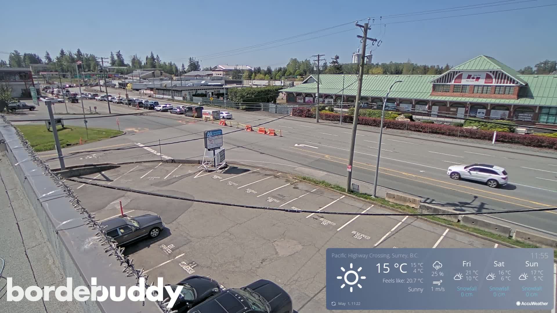 A sunny, overhead view of a parking lot and road, with cars parked and driving, next to a large building.